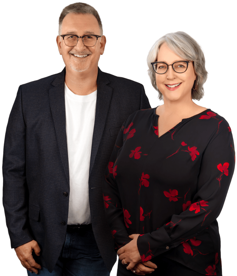 A professional and approachable portrait of Dale and CaroleAnn, featuring Dale in a smart casual blazer and CaroleAnn in a stylish floral blouse, both wearing glasses and offering welcoming smiles