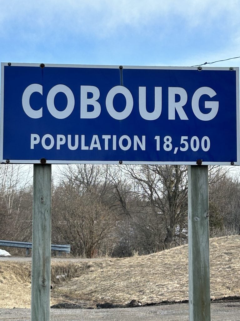 Cobourg Sign, prominently featuring bold lettering against a natural stone backdrop, surrounded by vibrant greenery, marking the entrance to Cobourg, Ontario.