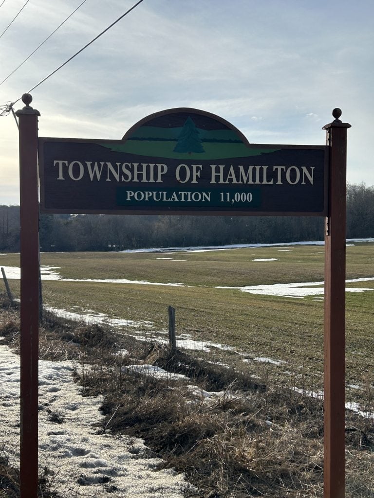 The Hamilton Township Sign, set against a rustic wooden background with bold, white lettering, marks the welcoming point to this dynamic and scenic area of Ontario, highlighted by its surrounding natural beauty.