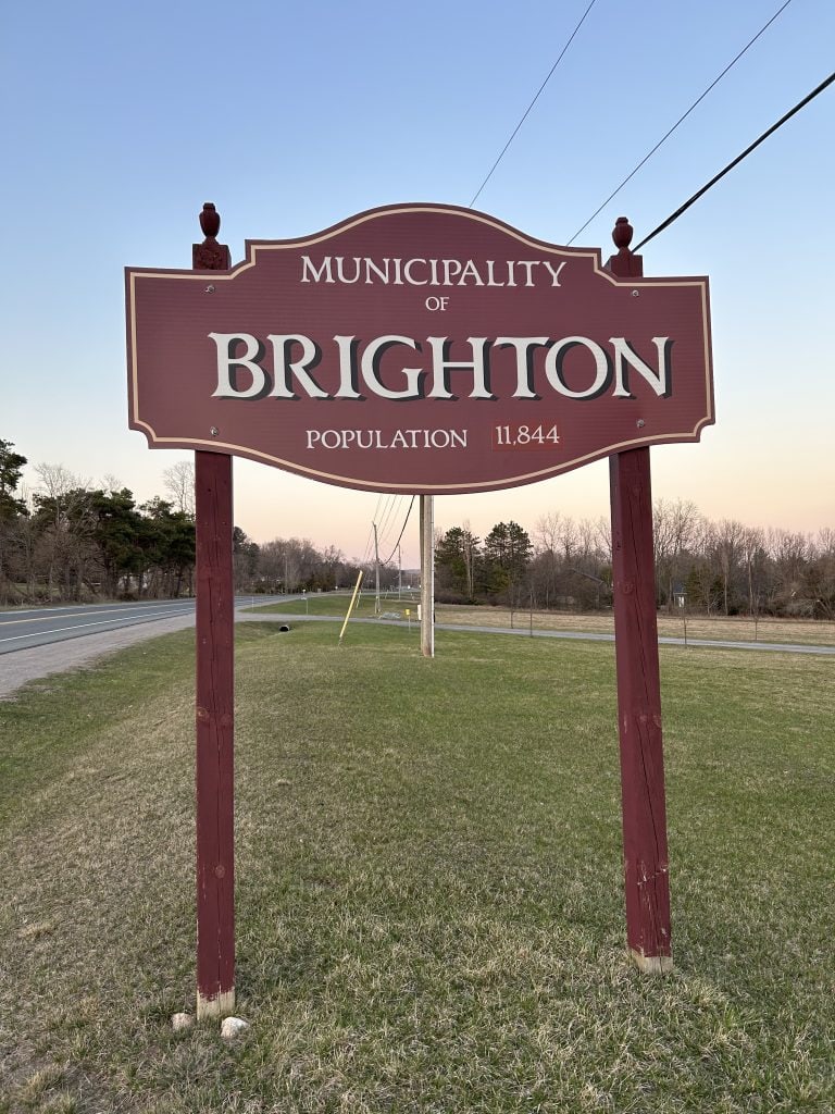 The Brighton Sign welcomes visitors with bold, white lettering set on a solid black background, complemented by surrounding greenery and a clear sky, marking the entrance to this charming Ontario community.