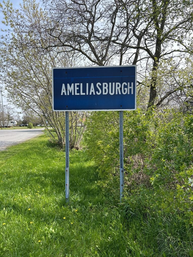 Ameliasburgh welcome sign surrounded by lush greenery under a clear blue sky in Ontario, Canada